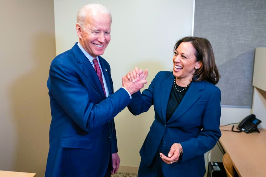 Joe Biden and Kamala Harris laughing and clasping hands