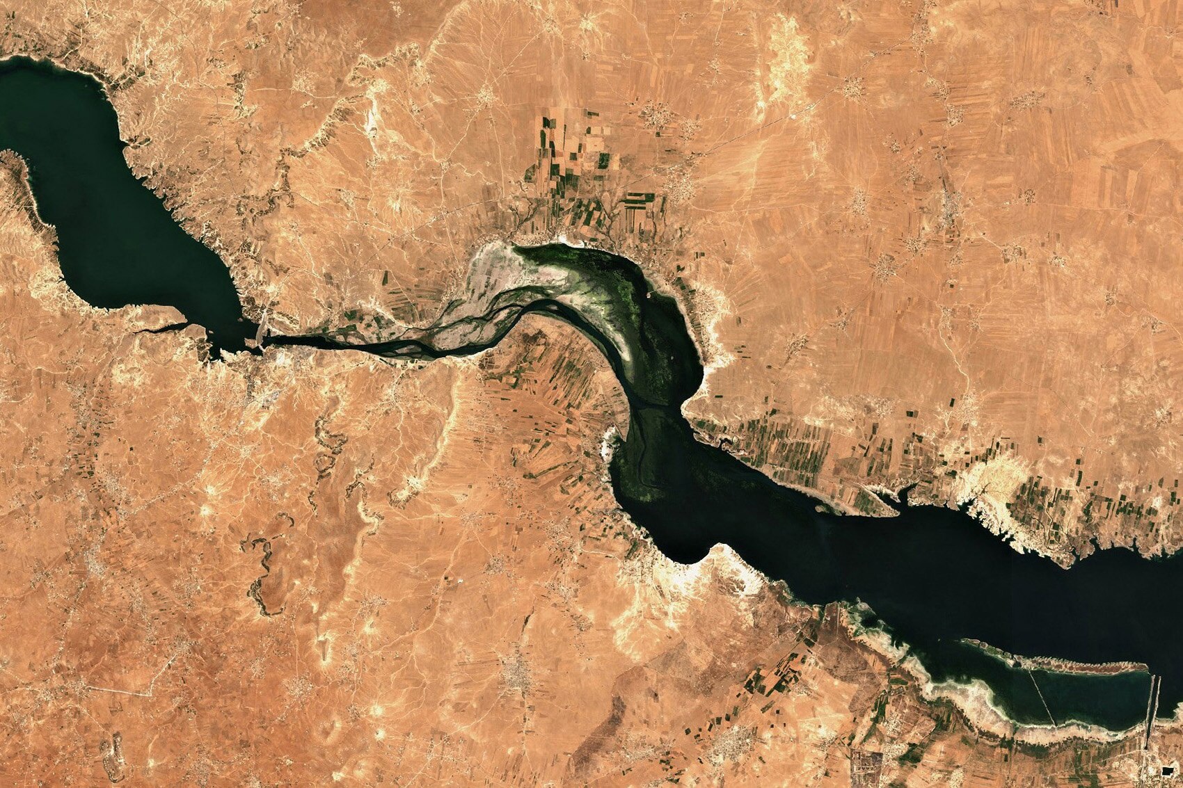 An aerial view of a thin water reservoir, seemingly surrounded by desert