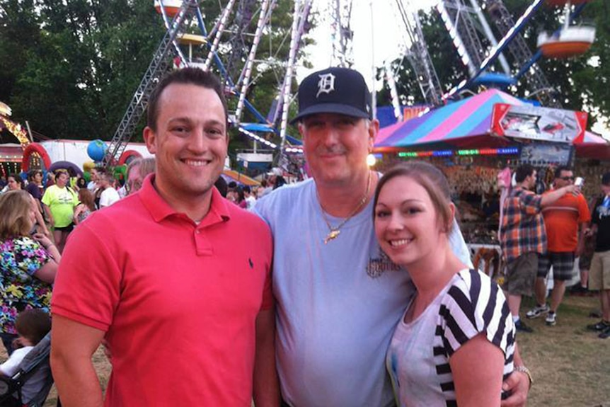 Two men and a woman pose for a photo at a fair. 