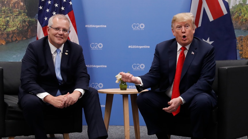 Donald Trump gestures at Scott Morrison, who is sitting beside him, with his thumb.