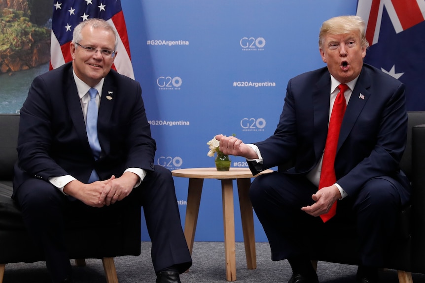 Donald Trump gestures at Scott Morrison, who is sitting beside him, with his thumb.