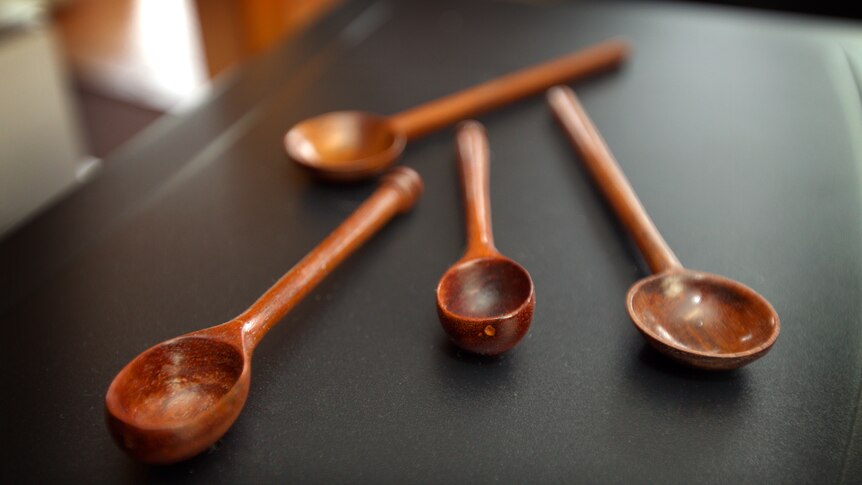 Four spoons made from dark timber sitting on a charcoal coloured surface.