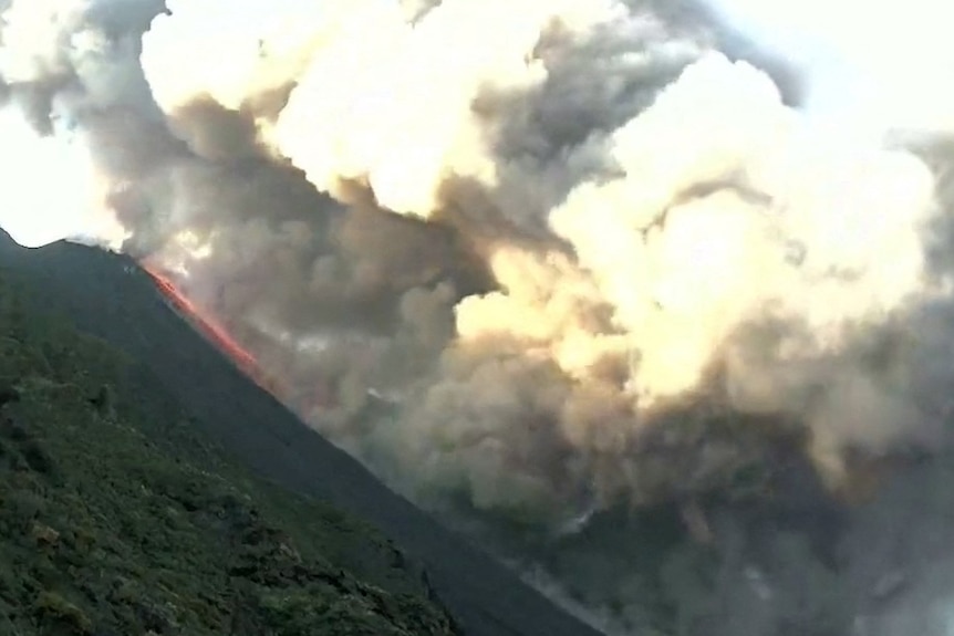 smoke pours from the volcano crater, where a thin bright red line of lava can be seen emerging