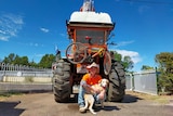 A young man and a dog sit in front of a tractor with a pushbike tied to the front.