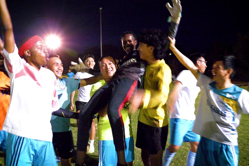 Ein junger afrikanisch-australischer Fußballspieler wird von seinen Kollegen gefeiert, sie halten ihn hoch und jubeln ihm zu.