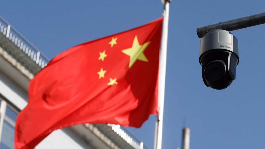 A round, black surveillance camera is pictured to the right of the Chinese flag outside.