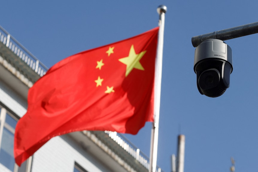 A round, black surveillance camera is pictured to the right of the Chinese flag outside.