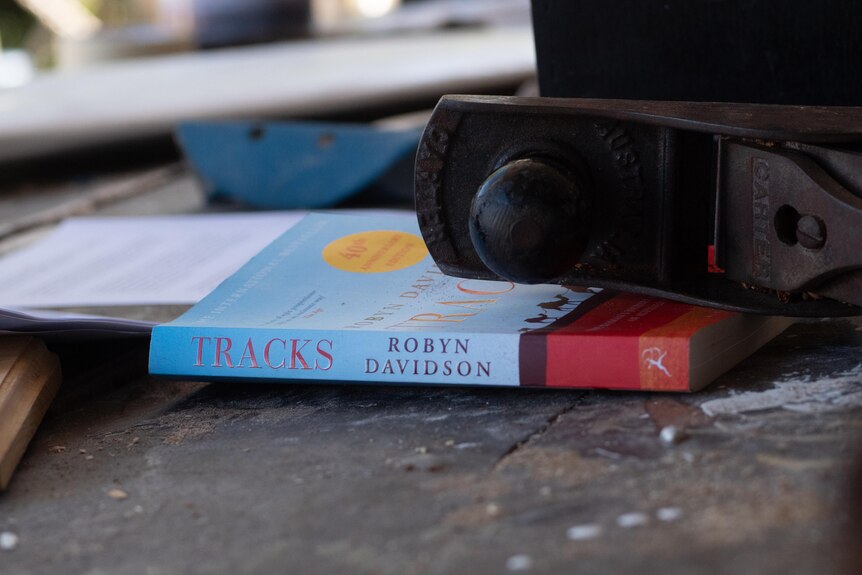 A book entitled Tracks, sits on a workbench with tools on top of it.