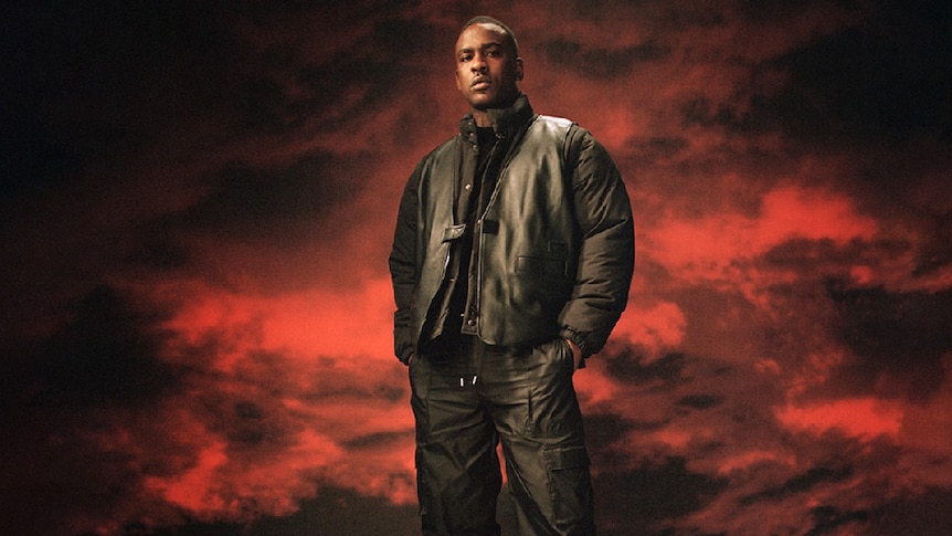 Image of rapper Skepra, dressed in all black, against a smoky red and black background