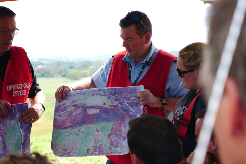 A man holds up an aerial map in front of fire fighters.