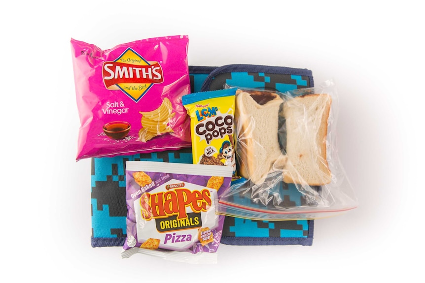 A Nutella sandwich, Coco Pops LCMs bar, salt and vinegar potato chips and pizza-flavoured shapes on top of a blue cooler bag.