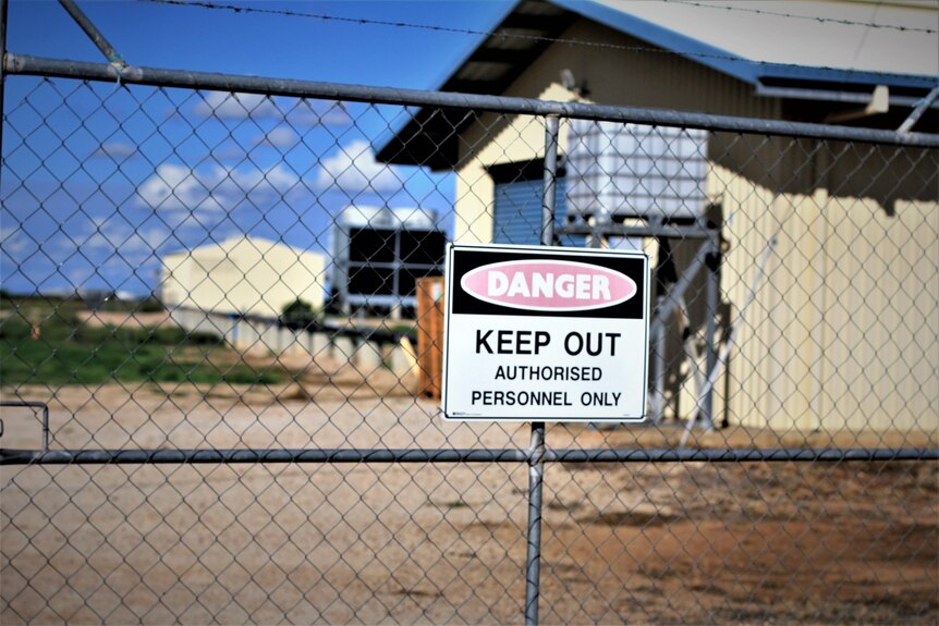 A "keep out" sign on a barbed wire fence surrounding a geothermal power plant.