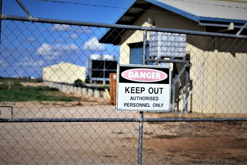 A keep out sign and barb wire fence surrounds a geothermal power plant