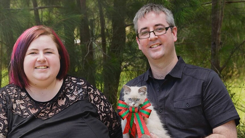 A woman with her partner and cat dressed in Christmas attire