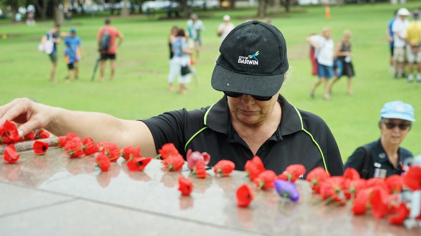 Woman places poppy on Darwin war memorial