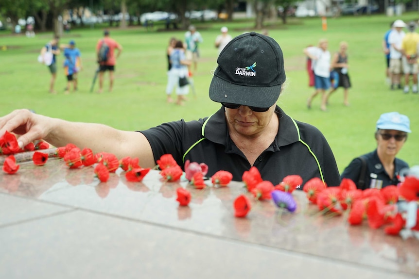 Woman places poppy on Darwin war memorial