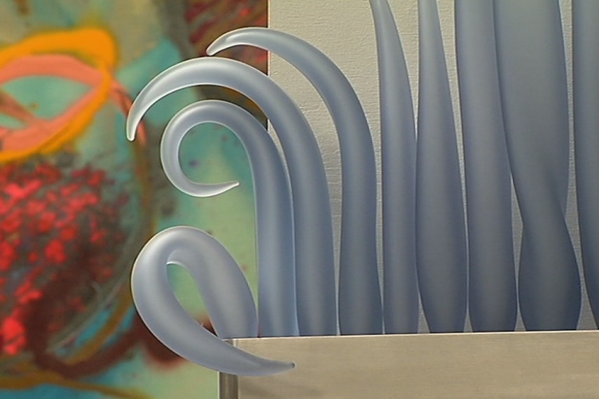 Curved blue glass in the shape of waves, mounted on a silver shelf.