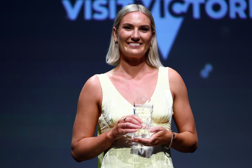 A wearing wearing a white dress poses with a glass award.