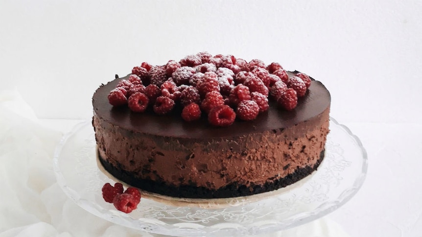 A chocolate torte with raspberries on top, sitting on a glass dish.