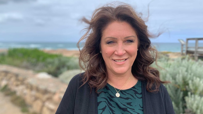 A middle-aged woman looking past the camera with a beach in the background