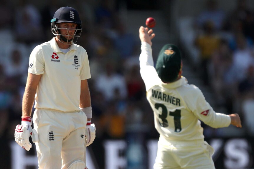 Joe Root looks frustrated. Out of focus, David Warner hurls the ball into the air in celebration.