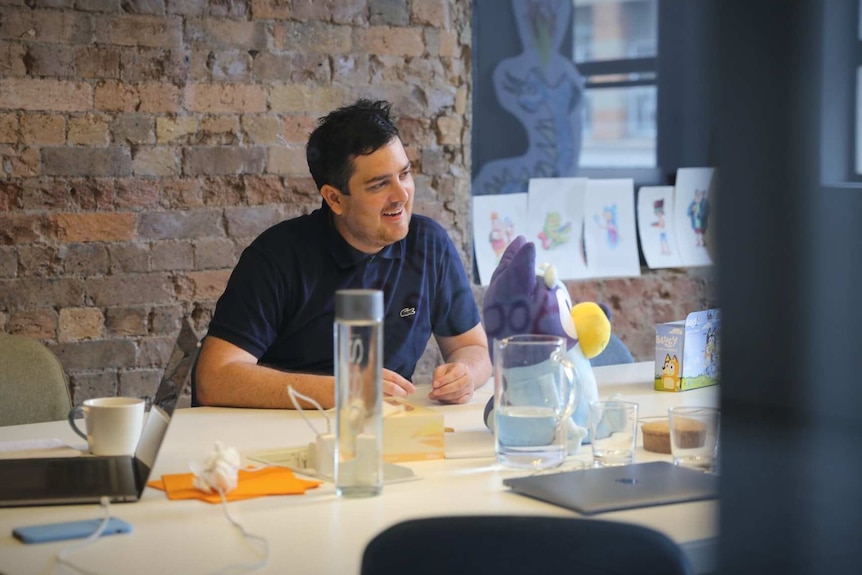 A man seen through the glass wall of an office smiling in a meeting.