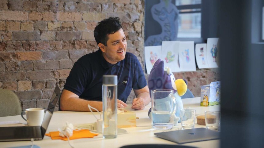 A man seen through the glass wall of an office smiling in a meeting.