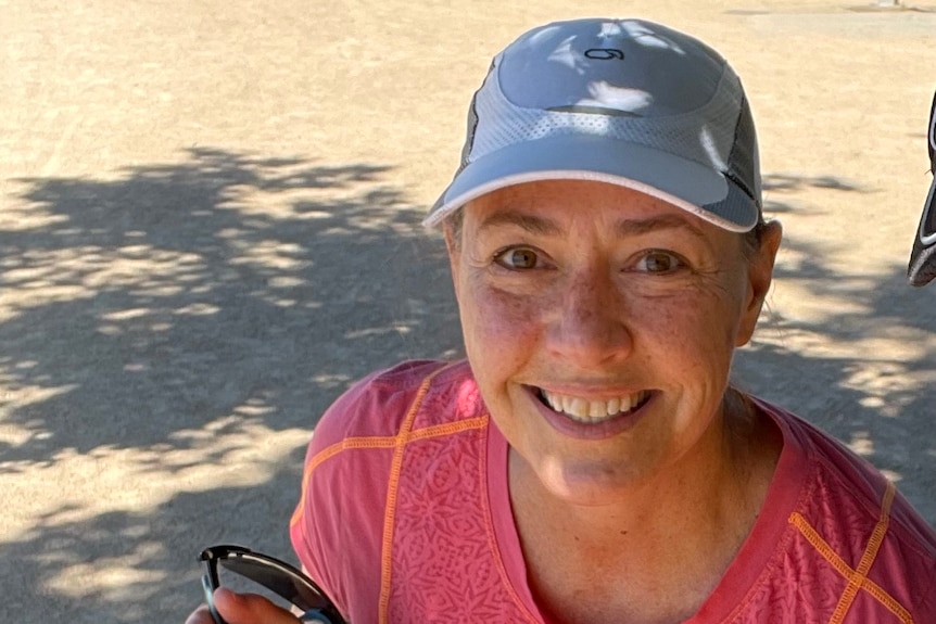 Lisa Millar, with sports cap and running shirt, smiles looking up, with parkland behind her.