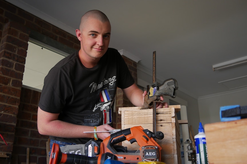 A man stands over a wooden box on a work bench