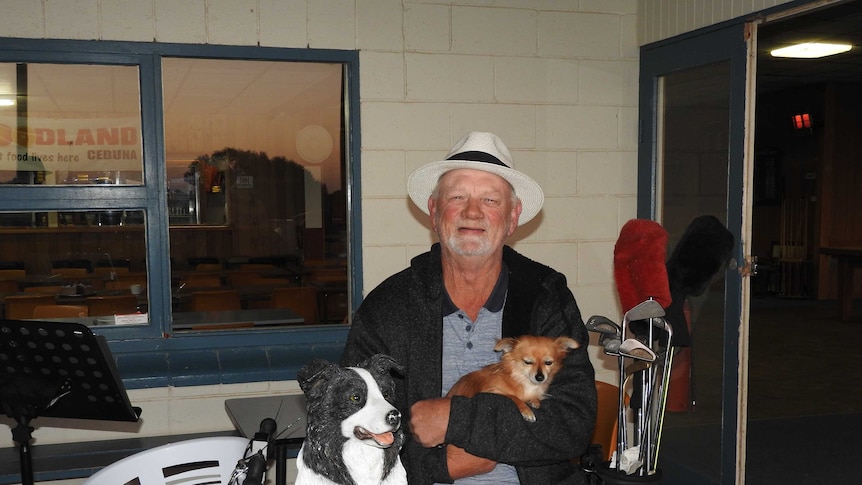 A middle-aged musician in a white hat holding his pet dog