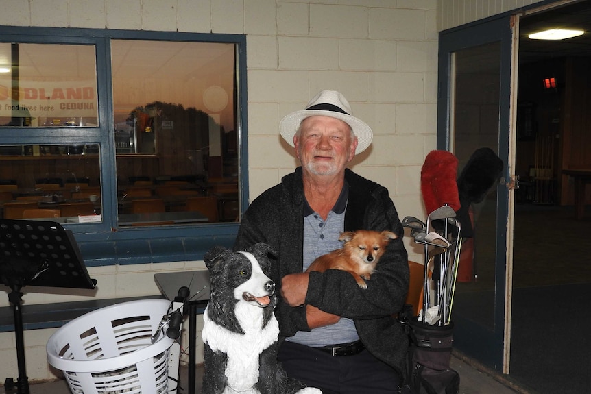 A middle-aged musician in a white hat holding his pet dog