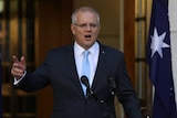 The Prime Minister holds his right hand up as he stands in the Prime Minister's courtyard