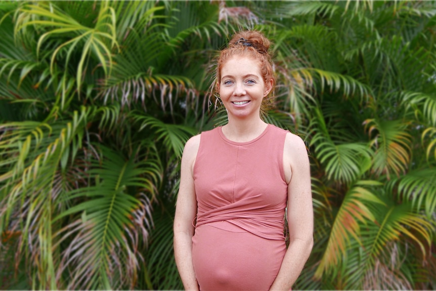 pregnant woman in red dress stands in front of green plants