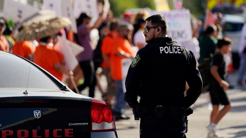 A Uvalde police officer watches as family and friends of those killed and injured in the school shootings protest.