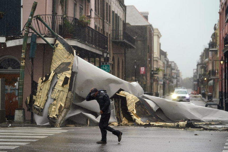 A man covers his head from the rain as he passes a section of roof that has been torn off a building by hurricane winds.