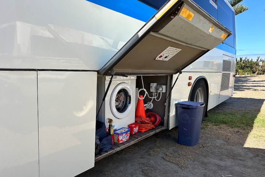The storage compartment of a bus is lifted open with a washing machine inside