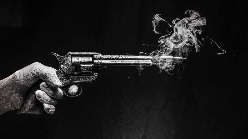 Picture of an old fashioned gun held by a hand, smoke coming out, black background, hand and gun are covered in white paint