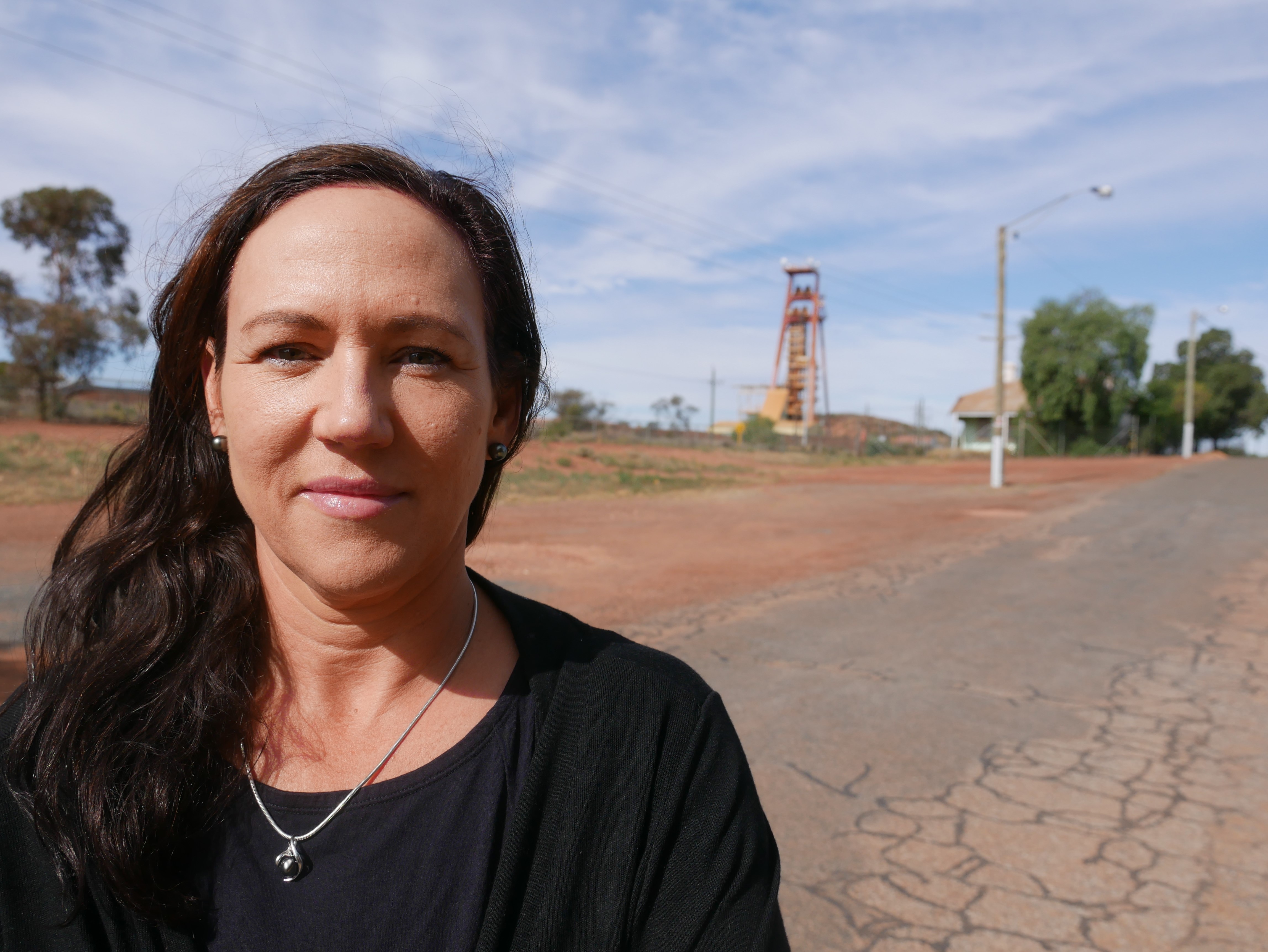 A woman wearing a black top smiles, with a road behind her.