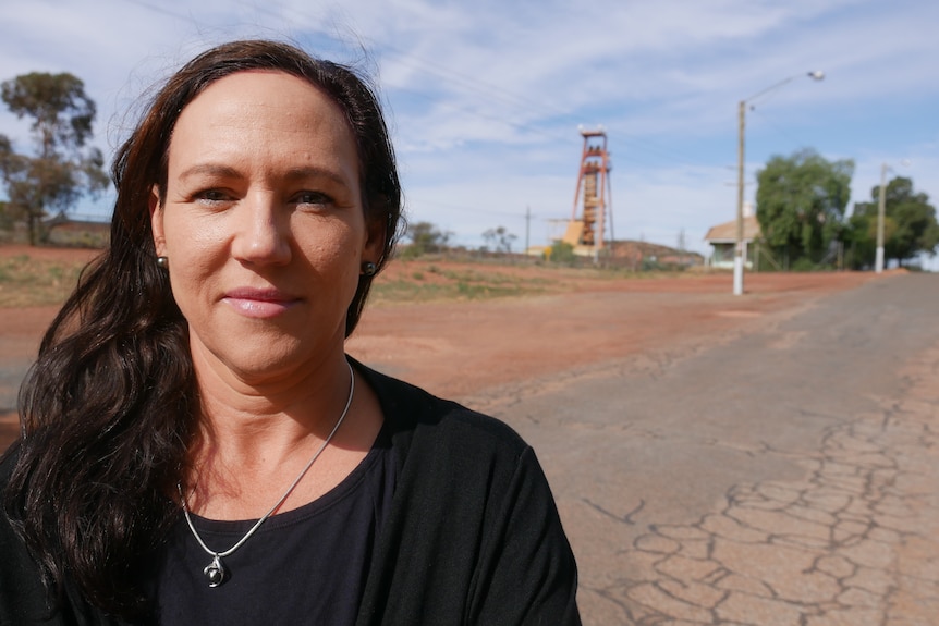 A woman wearing a black top smiles, with a road behind her.