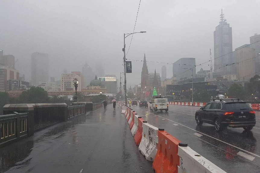 Melbourne's skyline is obscured by heavy grey fog. Cars on the road have their headlights on.