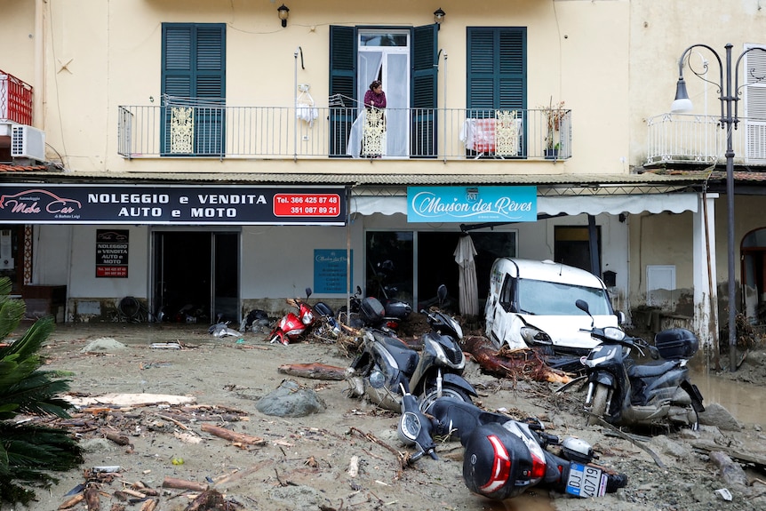 A woman looks from a balcony at a street covered in debris.