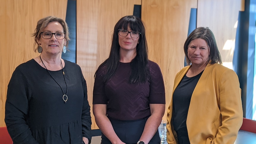 Three women stand together and look seriously at the camera