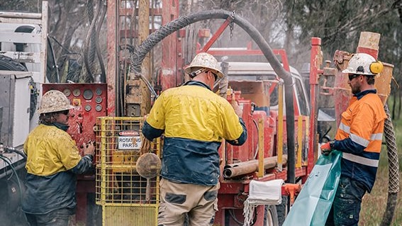 Three men operating a rig that's drilling into the ground