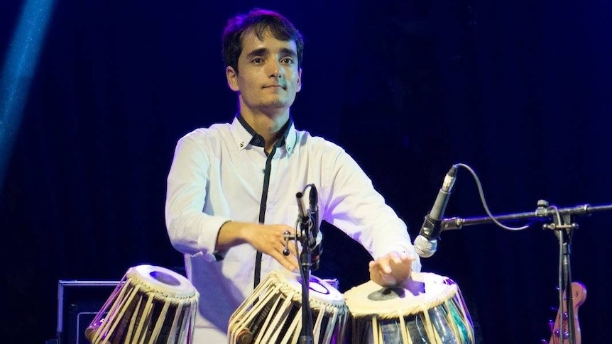 A young man plays the traditional tabla instrument while on stage