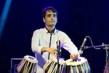 A young man plays the traditional tabla instrument while on stage