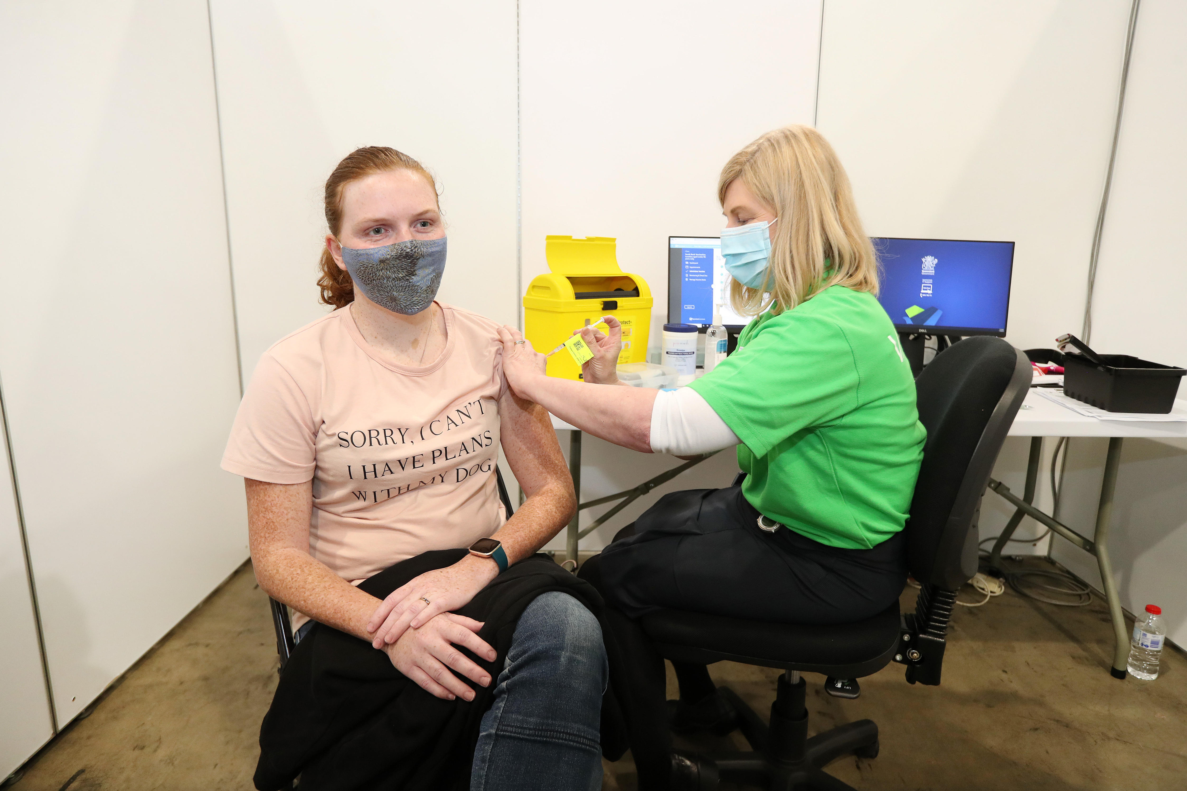 A doctor gives a vaccine to a young woman in a surgical mask in an office