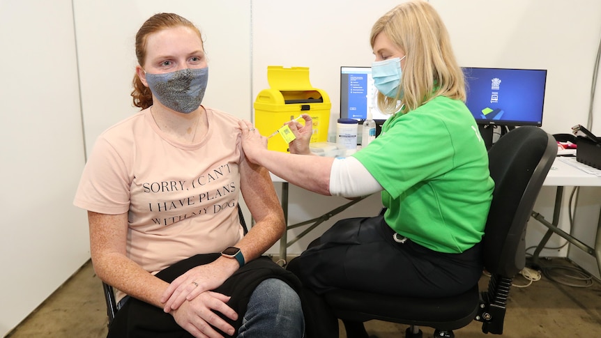 A doctor gives a vaccine to a young woman in a surgical mask in an office