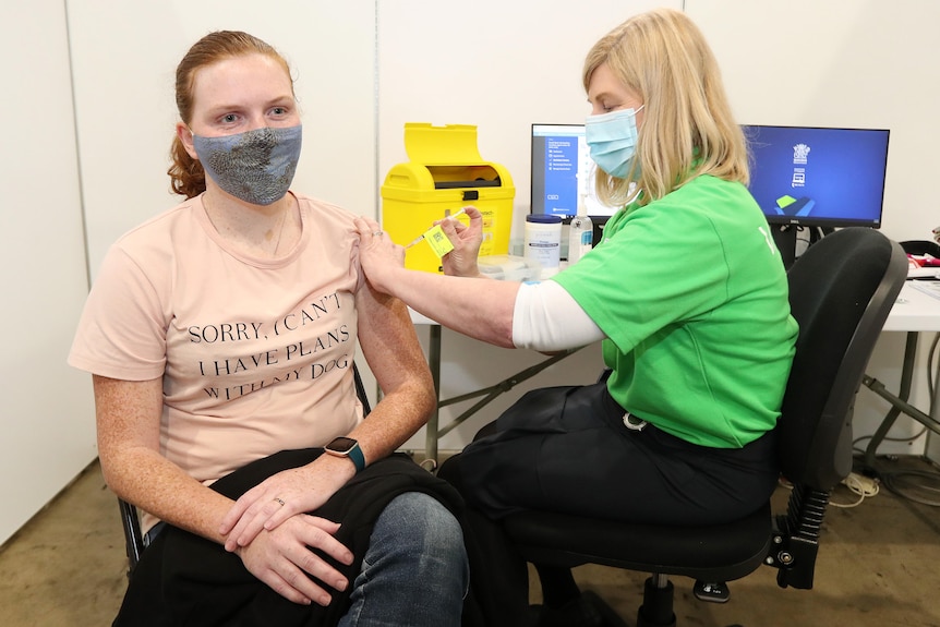 A doctor gives a vaccine to a young woman in a surgical mask in an office