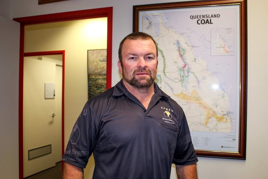 Steven Smyth in a CFMEU polo shirt standing in his office in front of a map, which says "Queensland Coal" on it.