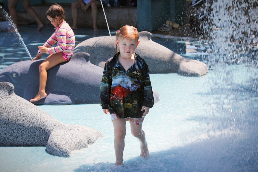 Two young girls play in a water park in the sunshine